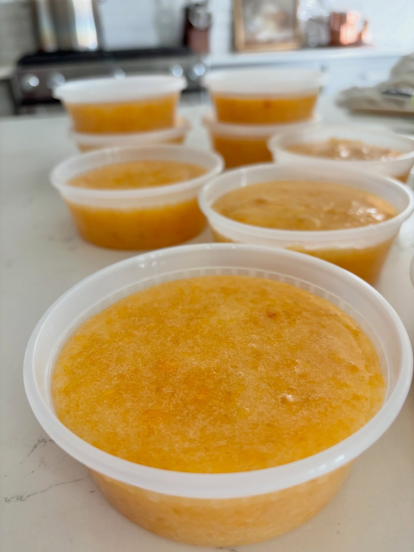 Tubs of golden peach freezer jam lined up on the counter