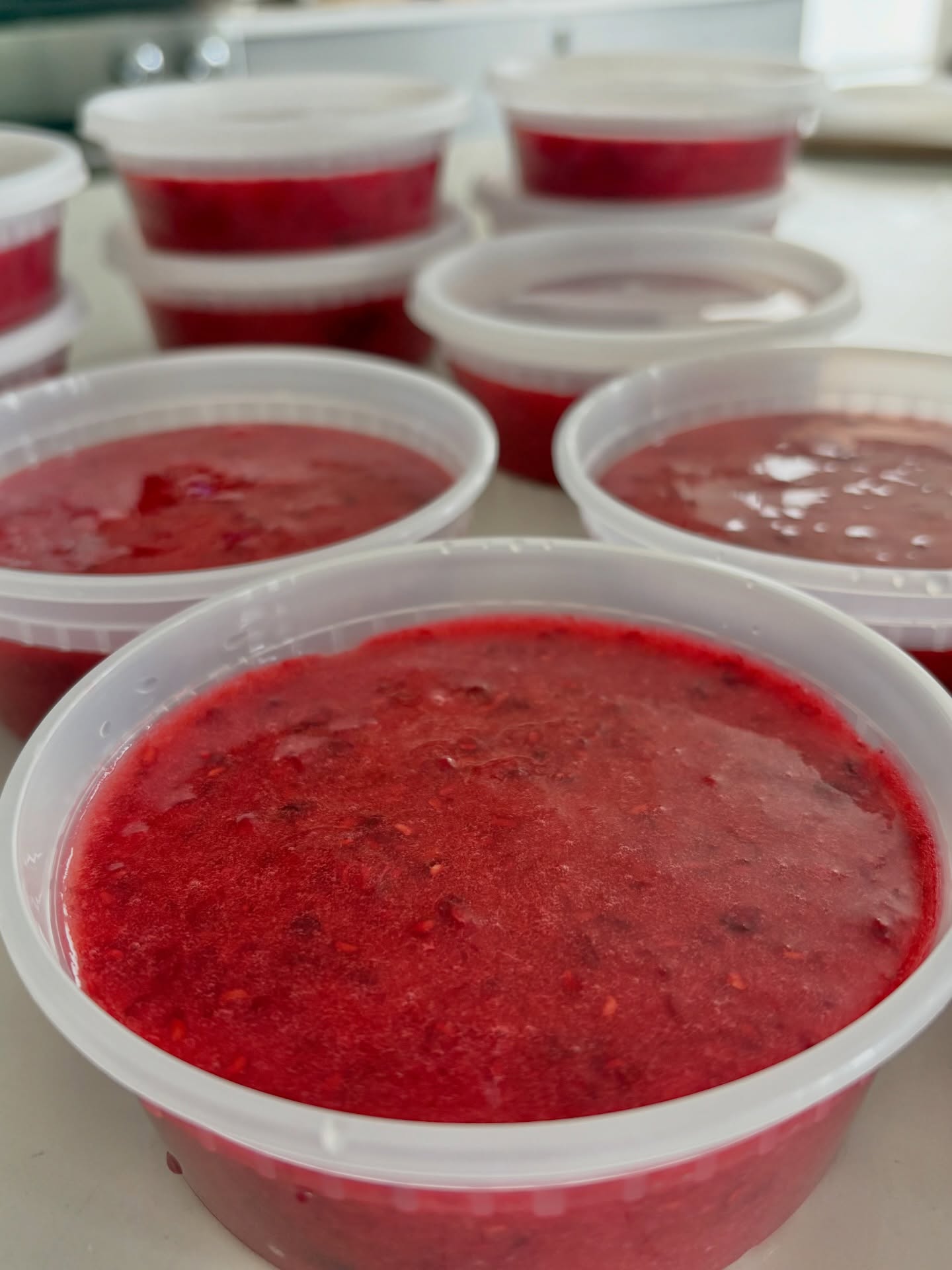 Tubs of freshly made strawberry freezer jam, deep red, ready for the freezer
