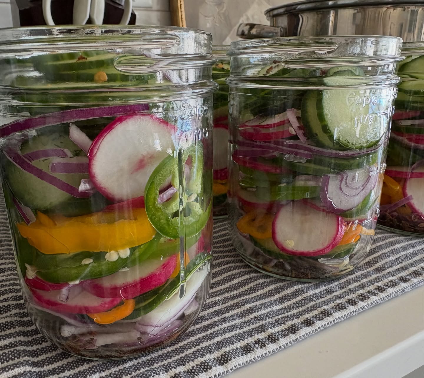 Mason jars packed with a colorful pickled spicy veggie mix — radish, cucumber, jalapeño and red onion