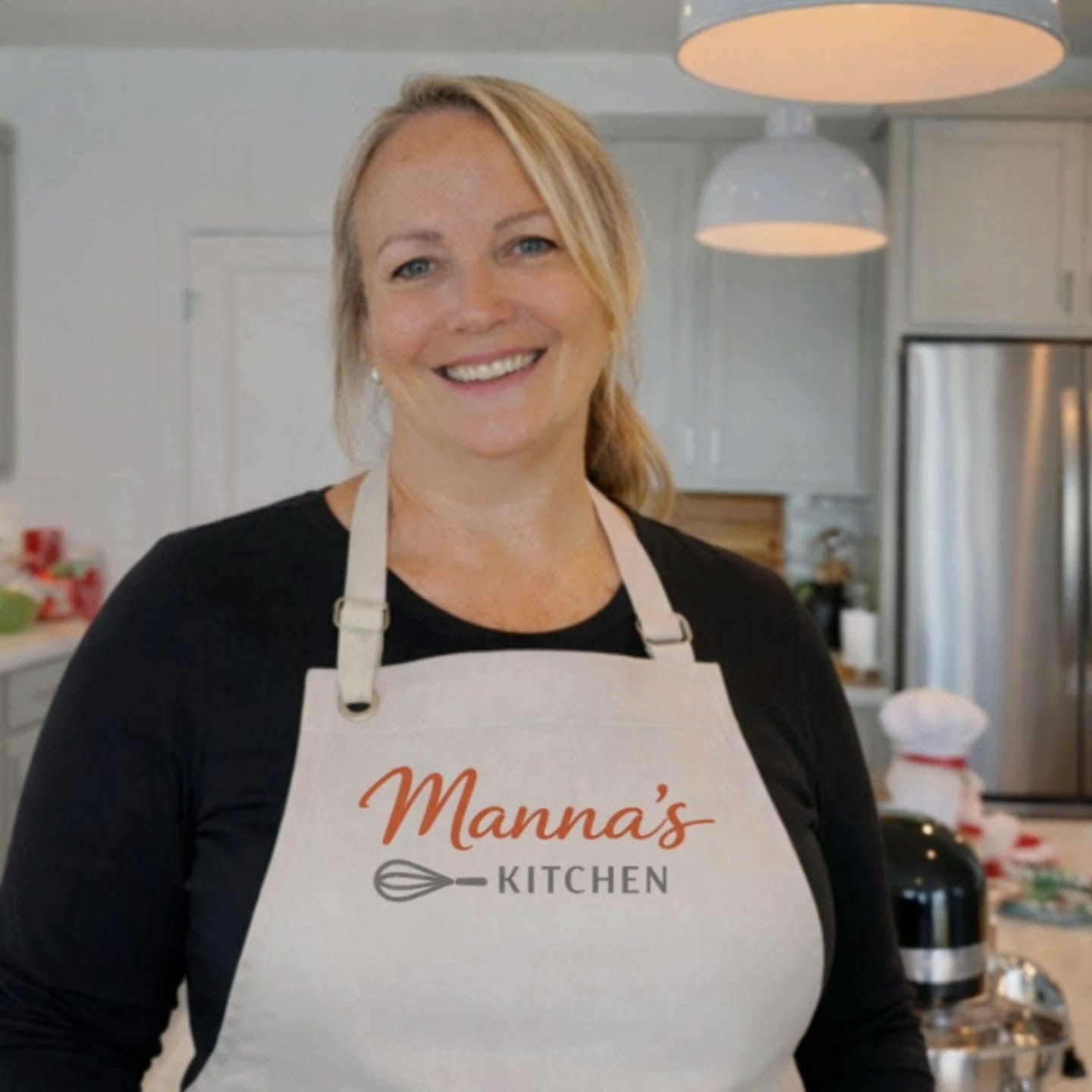 Rochelle, known as Manna, smiling in her bright kitchen wearing her Manna's Kitchen apron